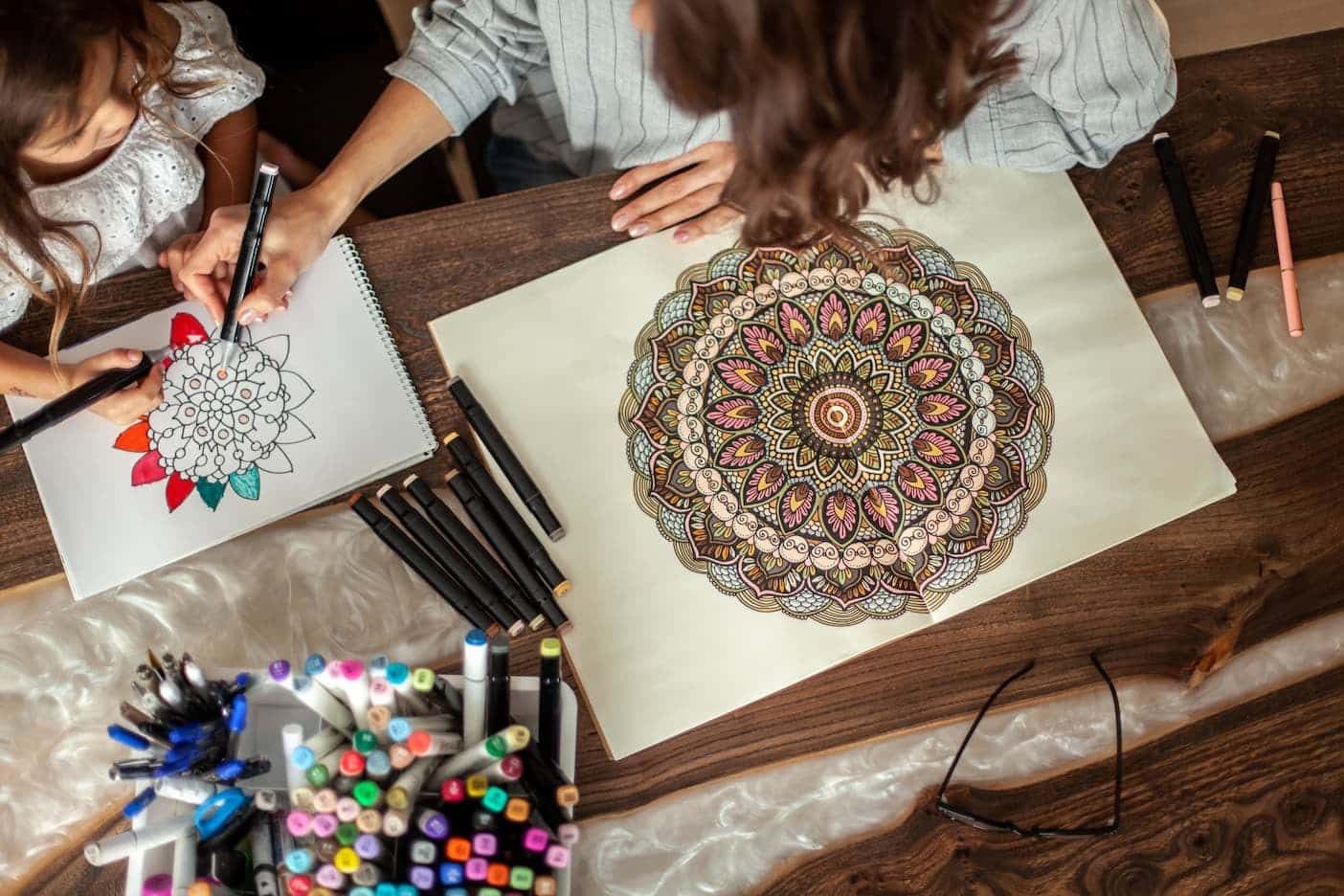 Hands coloring a detailed mandala with fine markers