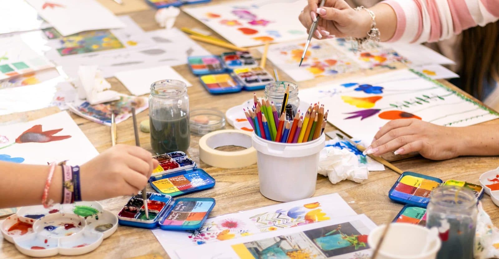 Workshop table set with watercolors, brushes and colored pencils