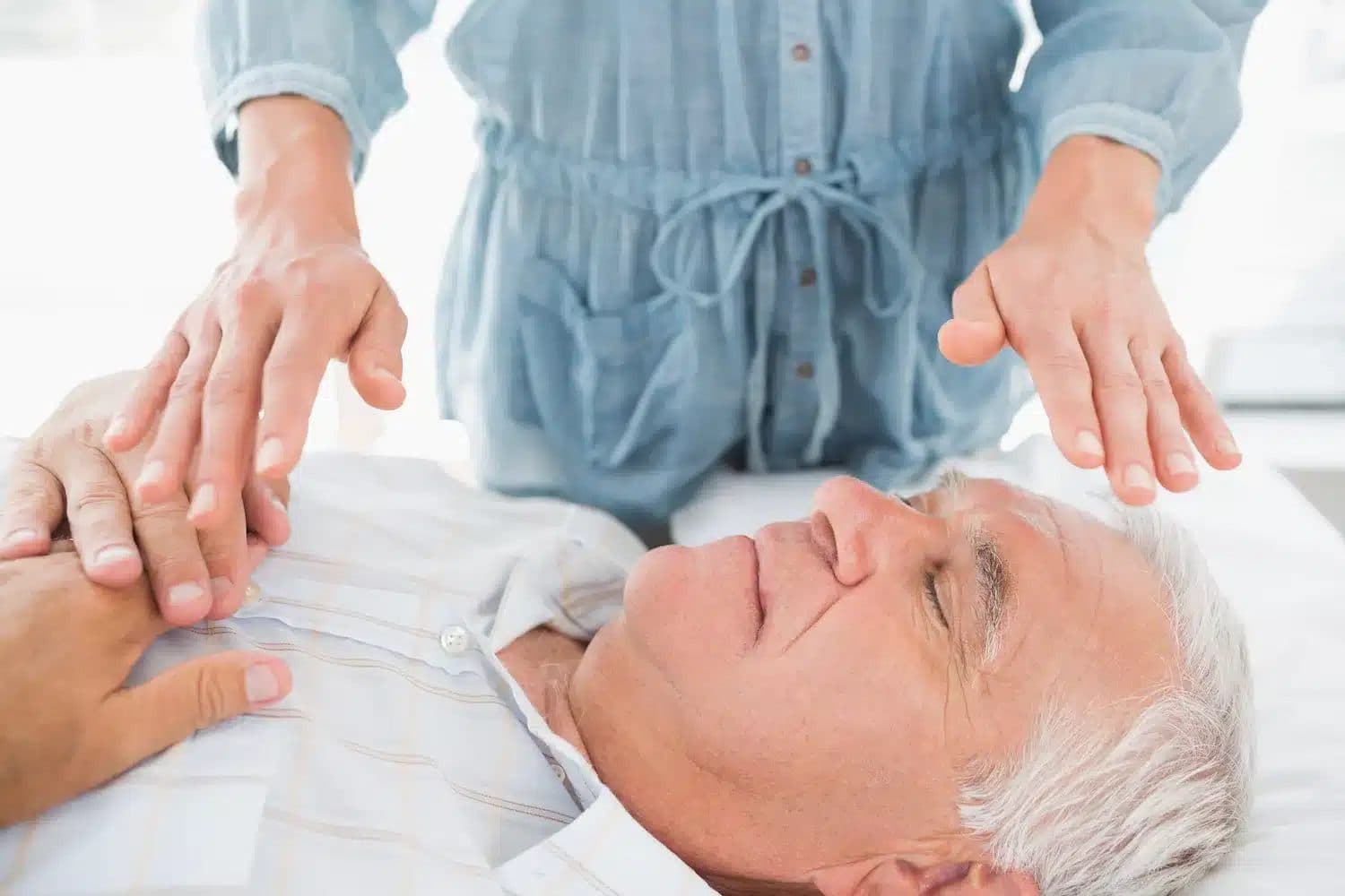 Hands working just above an older man's chest and face during an energy session